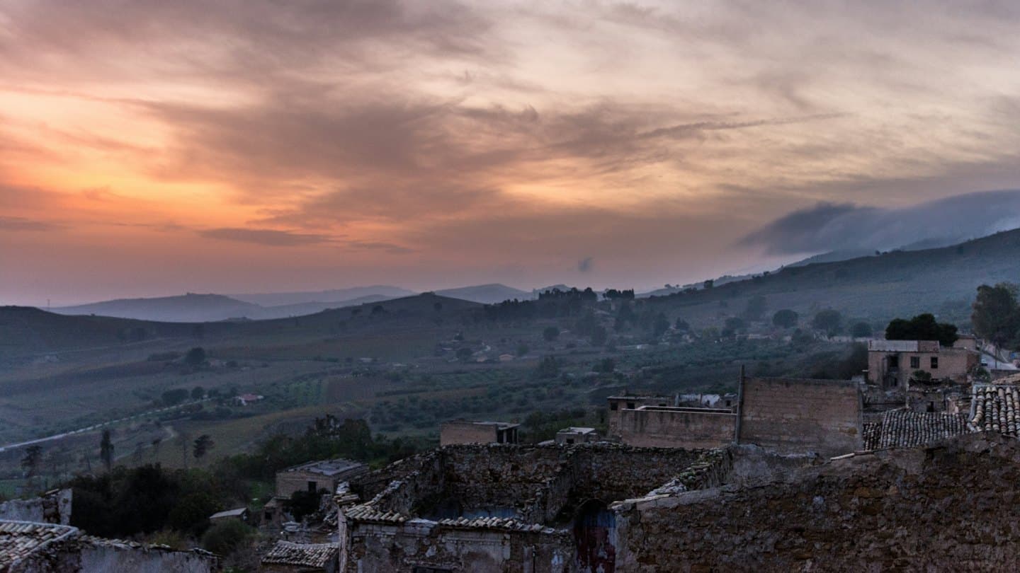 Rovine di pietra fatiscenti si affacciano su dolci colline in una valle rurale.