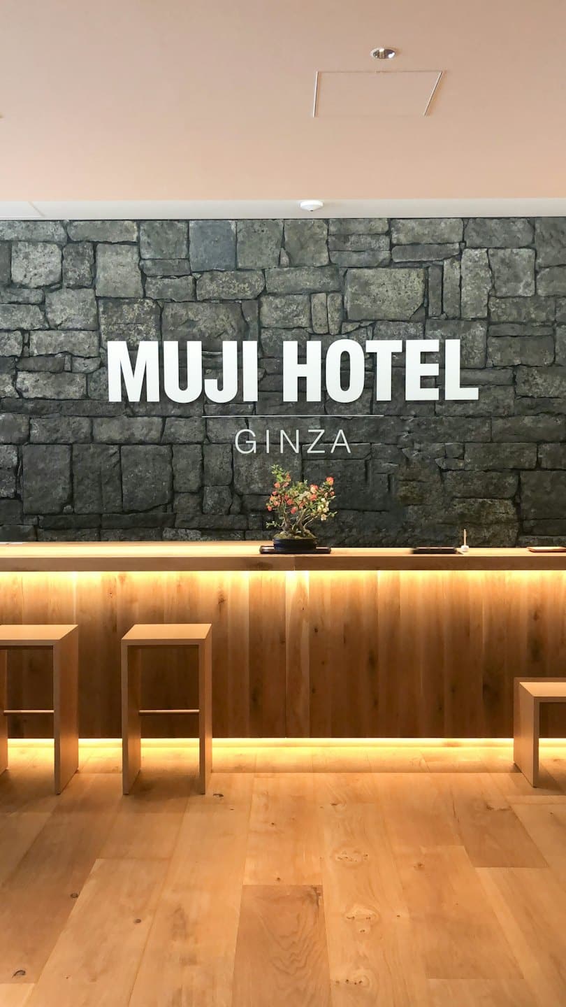 Reception dell'hotel con bancone in legno e parete in pietra grigia.