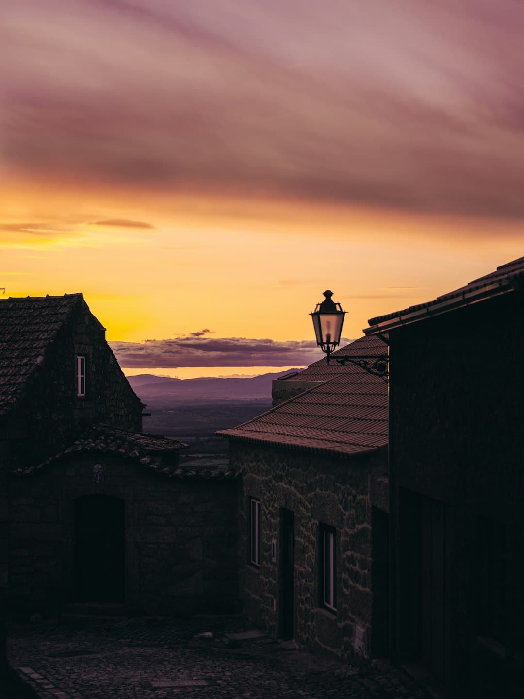 Edifici in pietra con tetti di tegole si affacciano su una valle nebbiosa al tramonto.