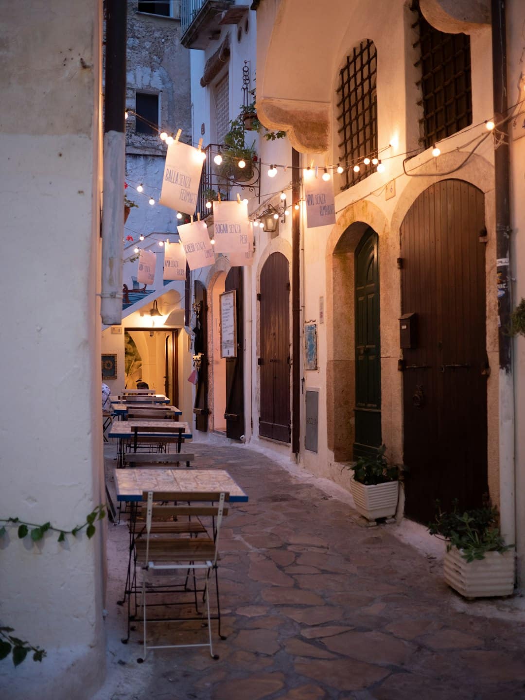 Tavoli da pranzo apparecchiati lungo una storica strada acciottolata di notte.