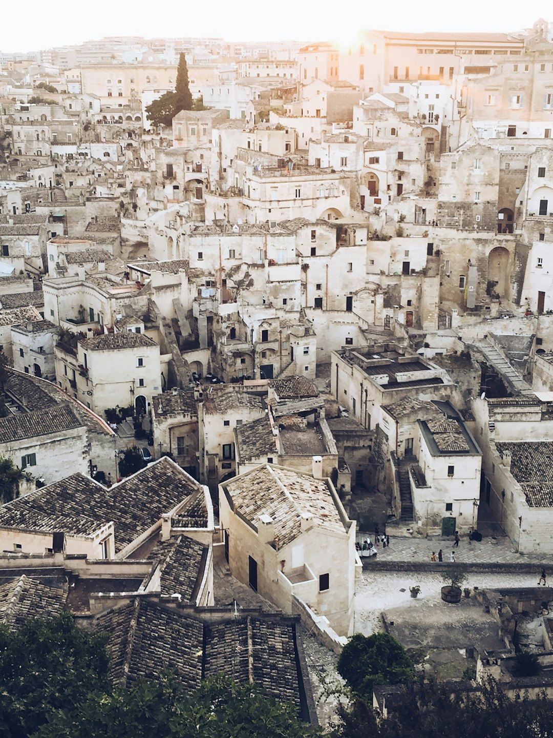 Paese collinare con edifici in pietra e tetti di terracotta al tramonto.